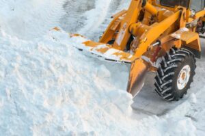 A front end loader scoops up a bucket of snow.