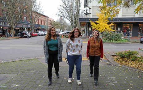 Three women walk on a downtown sidewalk.