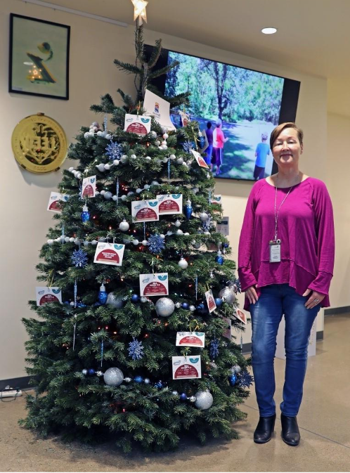 A woman with short hair poses near a holiday tree sprinkled with ornament-like cards